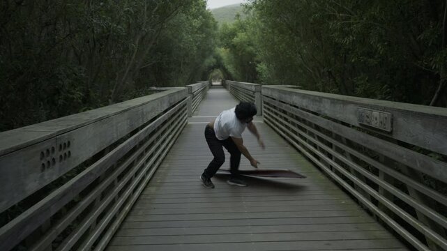 Man Doing Spin Trick with Painted Board And Dropping It On Wooden Footbridge
