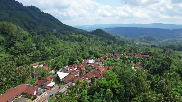 Aerial drone footage of an hidden local village in the middle of a valley, in Bruno area, Purworejo regency, Java island area, Indonesia, with forest around, touristic waterfalls behind