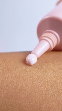 Moisturizing skin cream coming out from pink bottle packaging. Extreme vertical close up view. Beauty skincare product for daily hydration and care.