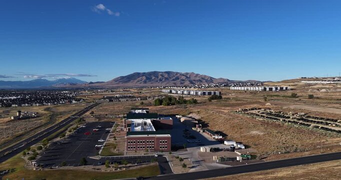 Aerial view of urban sprawl and modern development in the Utah Valley, featuring new buildings, roads, and dry landscape under a clear blue sky in Bluffdale, Utah, United States.