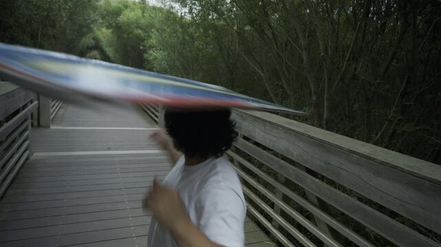 Athlete Spinning Red Painted Board On Head On Wooden Footbridge - Steady Cam Shot