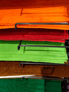 Stacks of colorful felt fabric sheets, paper in orange, red, green, brown, and blue on a metal shelf. Craft materials displayed in a store, ideal for art and DIY projects.
