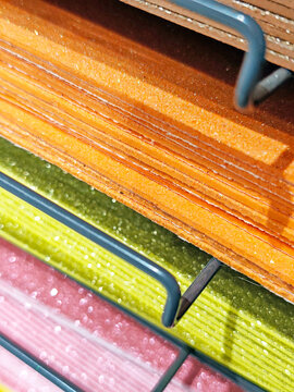 Stacks of colorful felt fabric sheets, paper in orange, red, green, brown, and blue on a metal shelf. Craft materials displayed in a store, ideal for art and DIY projects.
