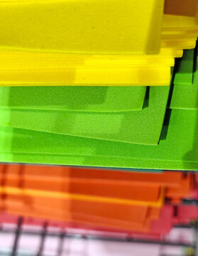 Stacks of colorful felt fabric sheets, paper in orange, red, green, brown, and blue on a metal shelf. Craft materials displayed in a store, ideal for art and DIY projects.
