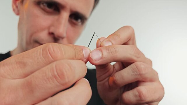 Man putting a thread through a needle eye 