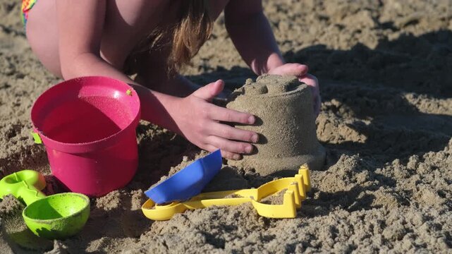 Close up young girl play with sand toys on beach. Summer vacation on ocean or sea coast concept. Kid having fun outdoors on family holidays. build sand castle