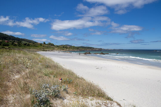 Praia de Carnota in A Coru&ntilde;a, Galicia, Spain. The image showcases the expansive white sand shoreline, gentle turquoise ocean waves breaking on the coast, and the dramatic silhouette of Monte Louro 