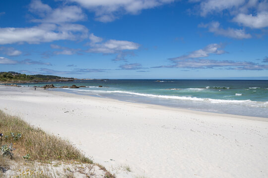 Praia de Carnota in A Coru&ntilde;a, Galicia, Spain. The image showcases the expansive white sand shoreline, gentle turquoise ocean waves breaking on the coast, and the dramatic silhouette of Monte Louro 