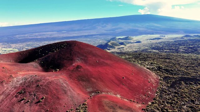 Aerial view of the Mauna Kea cinder cone and Mauna Loa volcano landscape featuring red volcanic soil and dark lava fields in Hawaii County, Hawaii, United States.