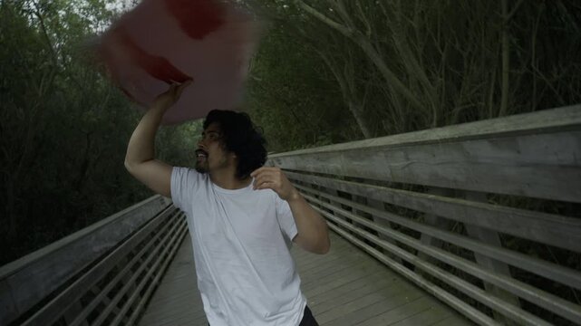 Man Tossing And Spinning Painted Board On Footbridge - Steady Cam Tilt Shot