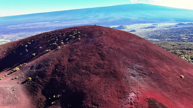 Aerial view of the Mauna Kea cinder cone and Mauna Loa volcano landscape featuring red volcanic soil and dark lava fields in Hawaii County, Hawaii, United States.