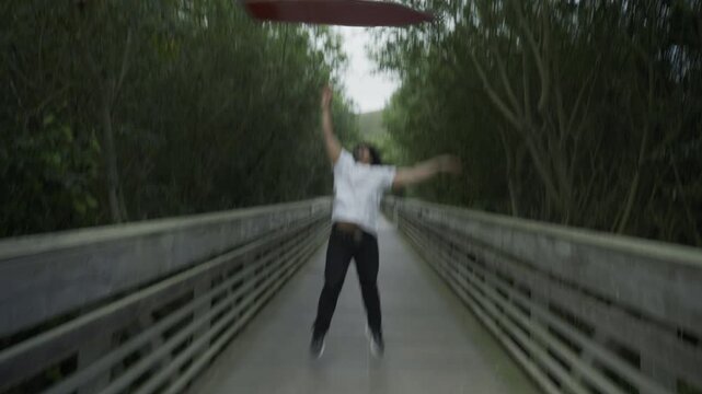 Man Spinning Painted Board Overhead on Wooden Footbridge And Tossing It Into Air - Steady Cam