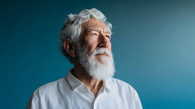 portrait of a distinguished older man with long gray beard and hair looking away against a calm blue studio background