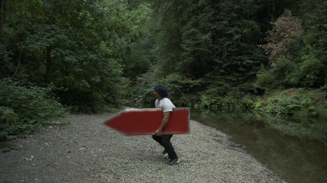 Wide Shot Of Man Throwing Colored Board Into Air, Doing Flip And Catching It Near Forest Stream