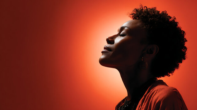 dramatic portrait of woman in silhouette showing natural afro hair against bold orange backdrop