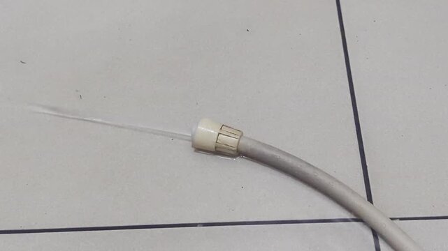 Close-up of water flowing from a disconnected toilet bidet spray flexible hose joint during maintenance