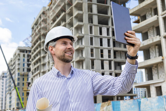 Construction engineer in helmet with the tablet pictures of objects on a construction site