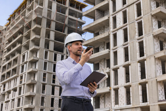 Engineer man in helmet use tablet computer for controls construction of skyscrapers, background buildings under construction.