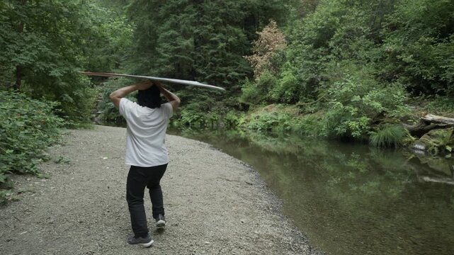 Man Spinning Painted Board And Doing Tricks on Gravel Shore Next to Forest Stream