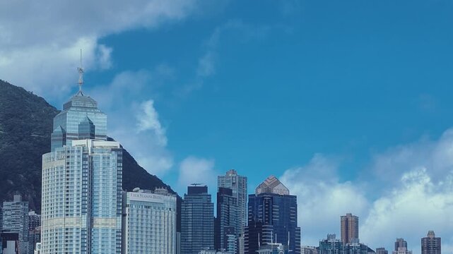 A sweeping view of the Hong Kong skyline with Tsim Sha Tsui district in the foreground and a lush green mountain range as a backdrop