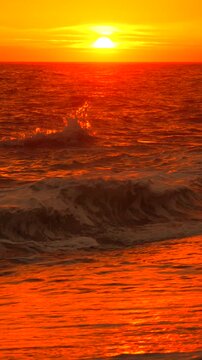 Sunset ocean waves reflecting vibrant orange light as the sun sets over the horizon of a peaceful coastal beach at dusk