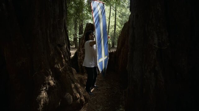 Silhouetted Man Waving Blue Cross Sign Between Large Redwood Trunks in Forest - Steady Cam