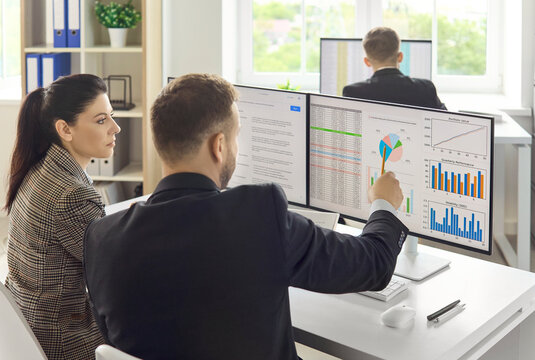 Businesspeople colleagues team meeting in office analytics data. Coworkers discuss market graphs on computer screens, pointing at charts. Concept of business analytics teamwork strategy.