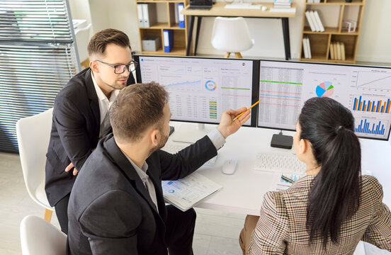 Businesspeople team meeting in office reviewing data. Colleagues view analytics and charts on screens, planning strategy and discussing decisions. Data strategy and teamwork discussion concept.