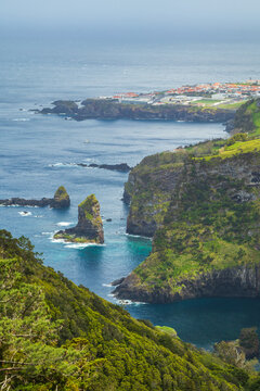 Impresionante vista panor&aacute;mica de islotes rocosos y acantilados cubiertos de vegetaci&oacute;n frondosa junto al oc&eacute;ano azul, con Santa Cruz al fondo. Flores, Azores.