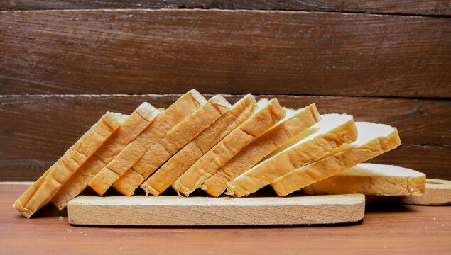 Fresh sliced bread arranged on a wooden cutting board over a rustic wooden table. Fresh delicious gourmet food background on the table rustic side view copy space.