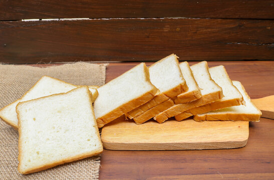 Fresh sliced ​​bread arranged on a wooden cutting board with one slice leaning against the stack over a rustic wooden table. top view copy space.