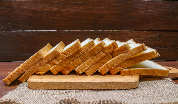 Fresh sliced bread arranged on a wooden cutting board over a rustic wooden table. Fresh delicious gourmet food background on the table rustic side view copy space.