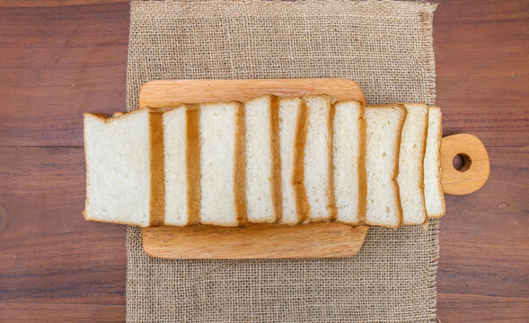 Fresh sliced ​​bread arranged on a wooden cutting board with one slice leaning against the stack over a rustic wooden table. top view copy space.