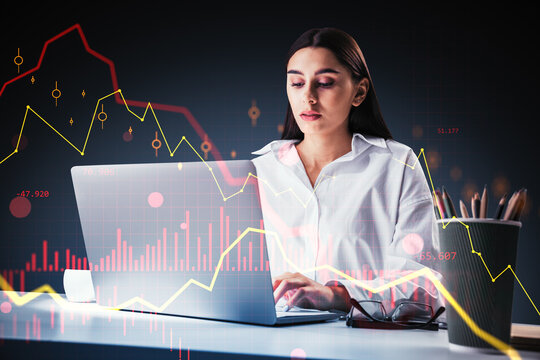 Focused businesswoman analyzing financial charts on laptop with digital market graph overlay in dark professional workspace environment.