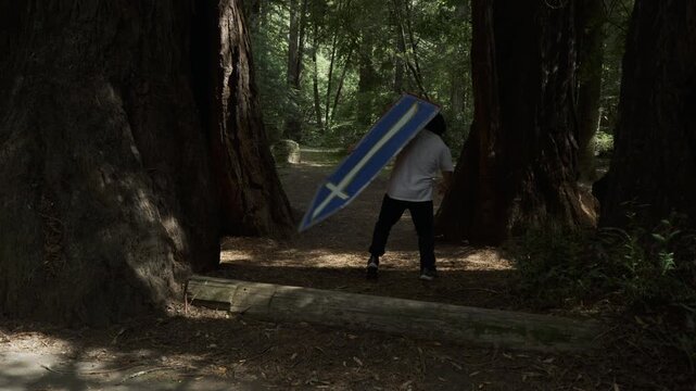 Man Carrying Blue Cross Board And Spinning It Through Redwood Path - Medium Shot