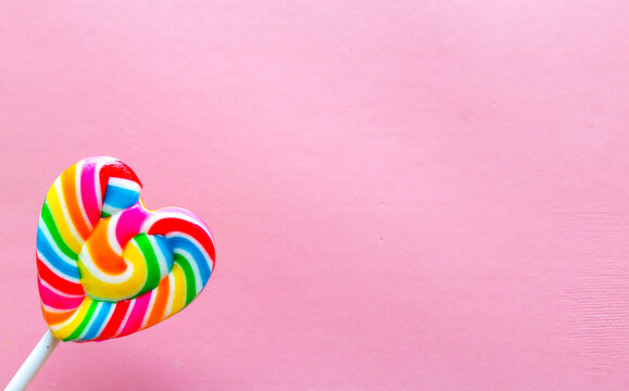 Colorful heart shaped lollipop isolated on pink background. Rainbow swirl candy with vibrant colors, sweet confectionery treat