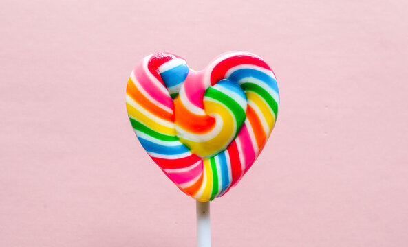 Colorful heart shaped lollipop isolated on pink background. Rainbow swirl candy with vibrant colors, sweet confectionery treat