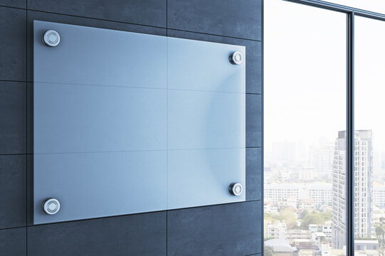 Empty modern interior with large blank glass sign mounted on dark wall beside bright city view window in contemporary business corridor. 3D Rendering