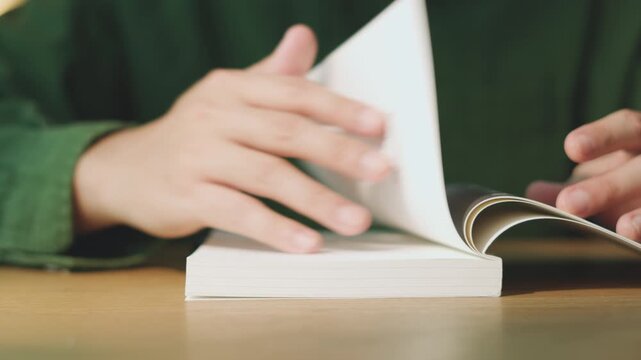 Close-up of Man Hands Turning Pages and Reading a Book on Wooden Table in the Morning routine. Education Study concept.