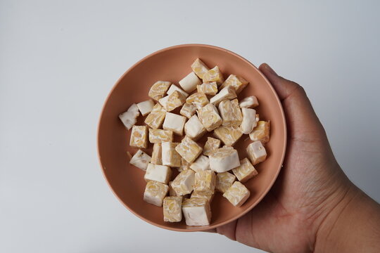 raw diced tempeh pieces on brown plate. cut tempe blocks. resh soybean tempeh cubes. tempeh food isolated background. hand holding bowl of tempe