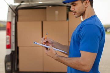 Delivery man with clipboard checking list and distribution of orders, standing by van full of cardboard boxes. Logistic, shipping service © Home-stock