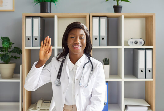 Female african american doctor looking at camera and waving hand having online video call or conference with colleague or patient. Telemedicine and patient consultation online concept.