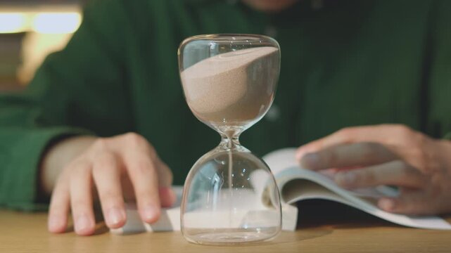 Closeup Turning Sandglass to Start Deep Work and Studying Literature in Cozy Room.