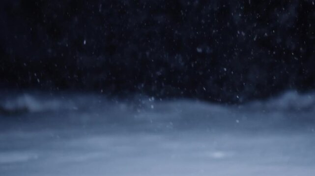 Falling snow particles on dark wintry background with blurry ground
