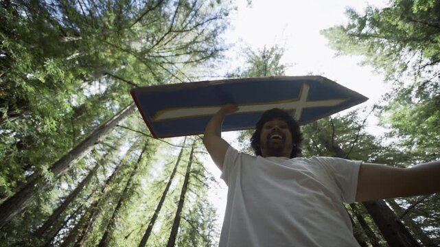 Man Raising Painted Board Overhead And Spinning It Among Redwood Canopy - Low Shot