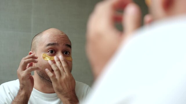 Man applying a sheet mask in front of a bathroom mirror during his morning skincare routine. Healthy aging longevity. Men self-care anti-aging skincare. wellness and preventive health concept.
