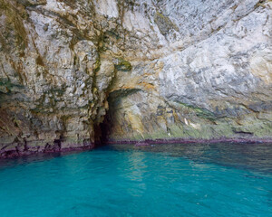 Fototapeta premium Rugged rock formation and steep limestone cliffs standing in the calm sea at Blue Grotto, Malta