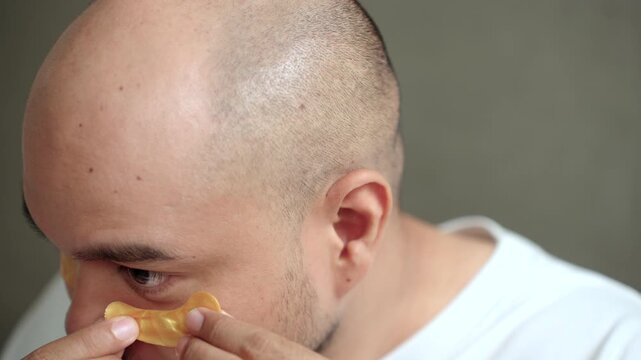 Close up man applying a sheet mask in front of a bathroom mirror during his morning skincare routine. Healthy aging longevity. Men self-care anti-aging skincare. wellness and preventive health.
