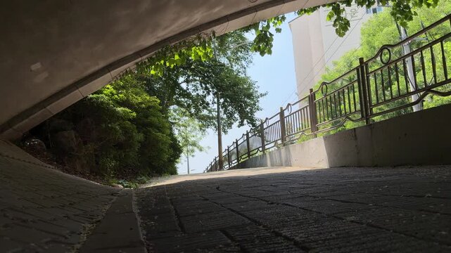 Low angle tracking shot walking out of a dark concrete underpass towards a bright sunlit city street