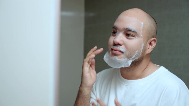 Man applying a sheet mask in front of a bathroom mirror during his morning skincare routine. Healthy aging longevity. Men self-care anti-aging skincare. wellness and preventive health concept.
